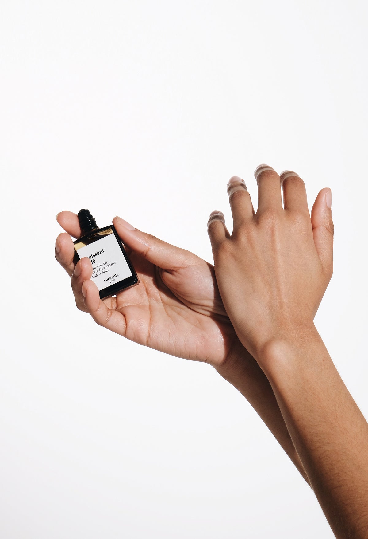 Mani che applicano un extrait de parfum roll-on Versatile Paris Immagine