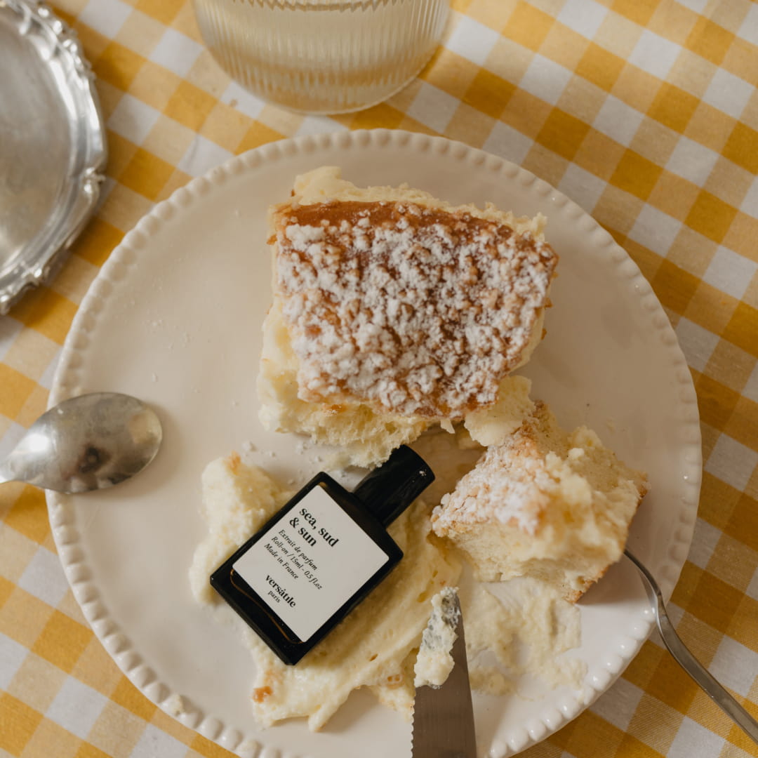 Flacon Sea, Sud & Sun de Versatile Paris sur une nappe vichy avec une part de tarte tropézienne
