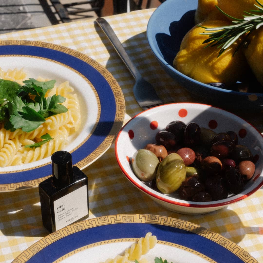 Flacon Rital Date de Versatile Paris sur une table d'été avec pâtes au pesto et olives